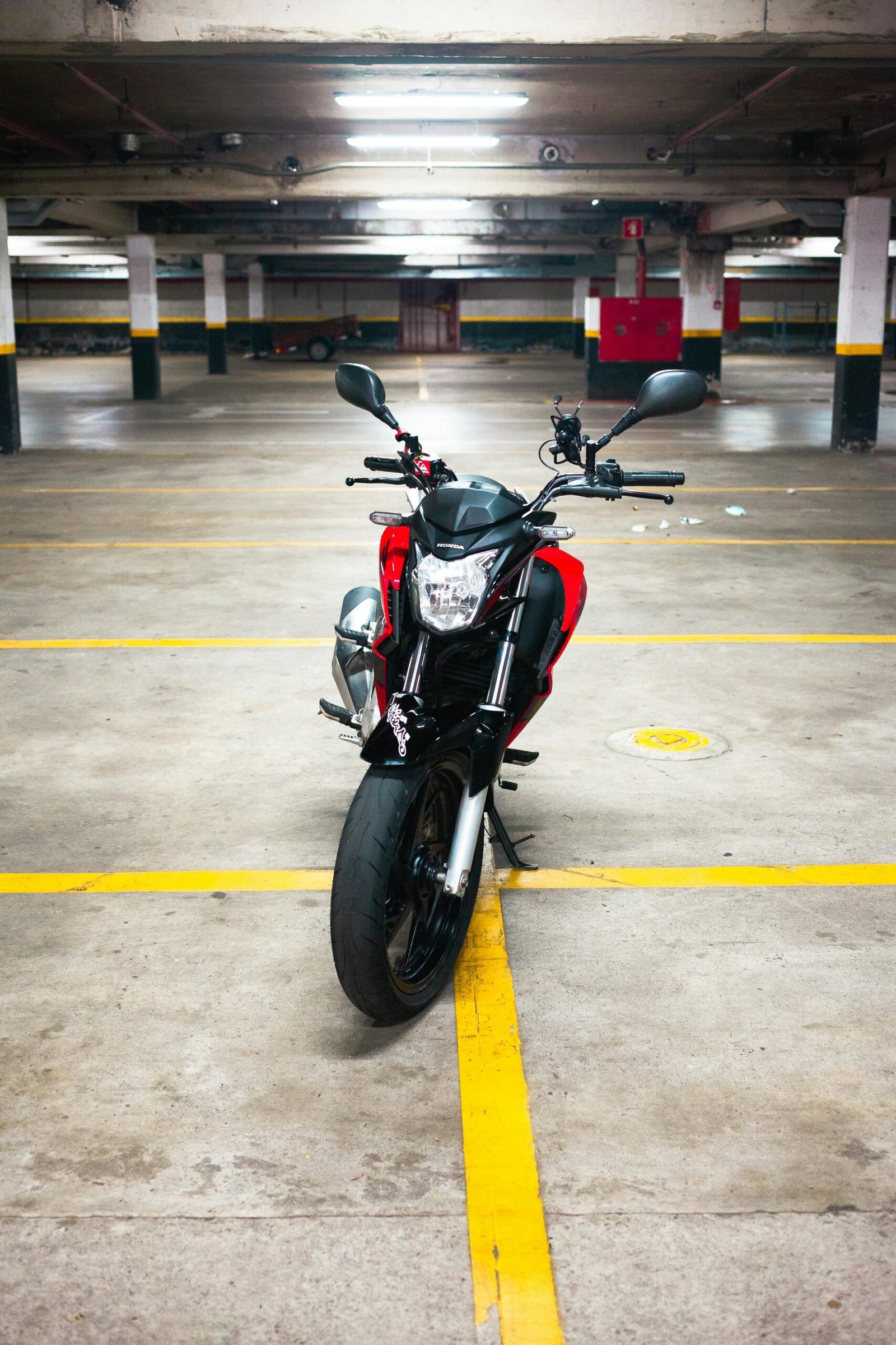 A red motorcycle stands alone in an empty underground parking lot.